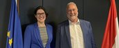 Martine Ouwersloot en Eduard Dame lachen in de camera, staand tussen de Europese vlag en de Nederlandse vlag