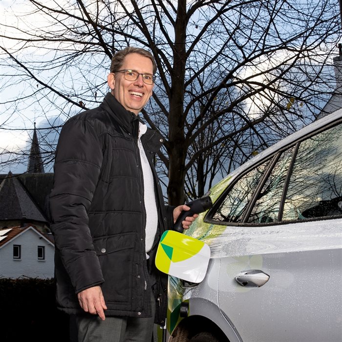 Wethouder Mark Gerritsen met een stekker in zijn hand, naast een elektrische auto