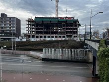 Betonnen karkas van nieuwe woontoren, met hijskraan op de achtergrond. Op de voorgrond loopt een weg die en tunnel in leidt.